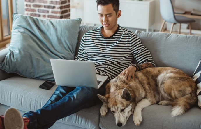 Man on couch with laptop and dog.
